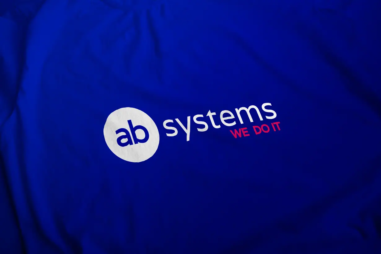 AB Systems: logo z białym kołem z literami ab, napisem systems i różowym hasłem WE DO IT na niebieskiej tkaninie
