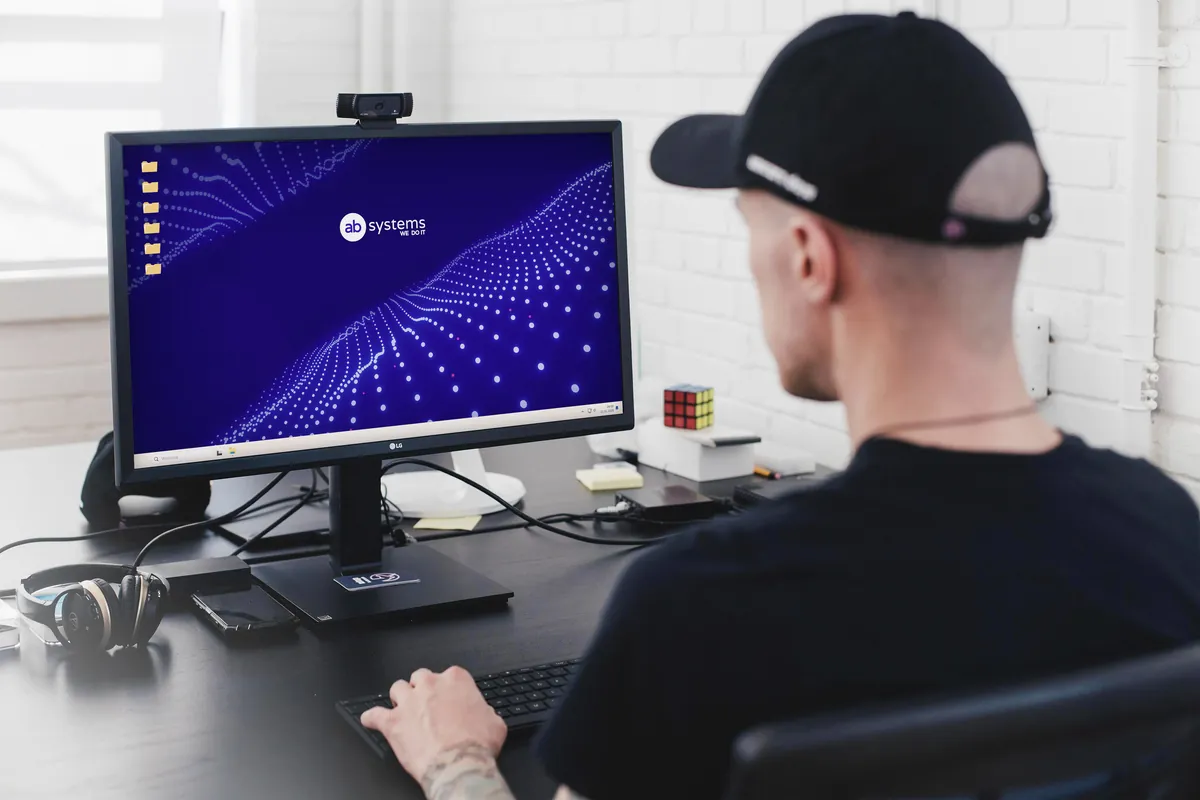 AB Systems: man at a desk in front of a monitor with a navy wallpaper with a wave of glowing points and the logo