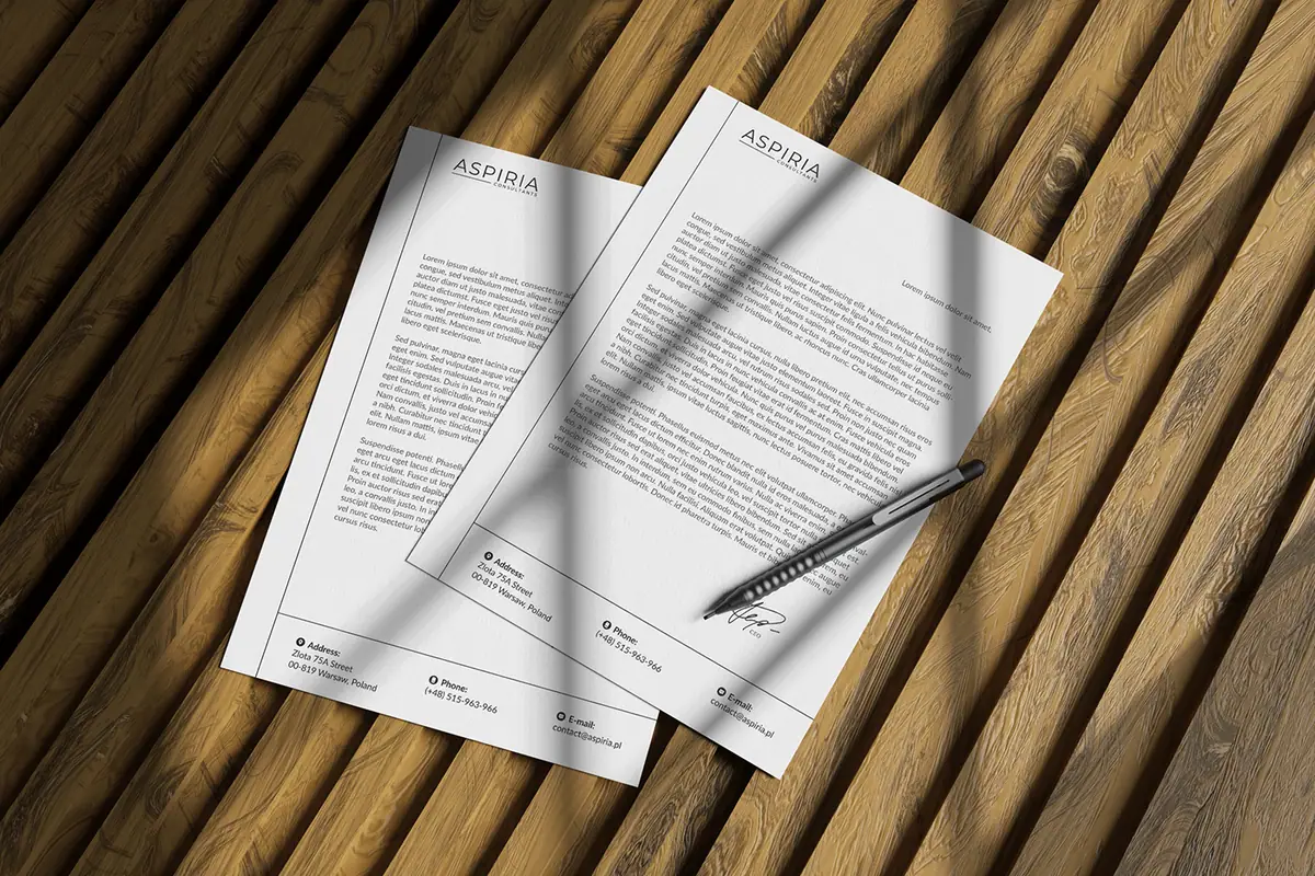 Aspiria: dwa arkusze papieru firmowego z logo i stopką adresową na drewnianym tle