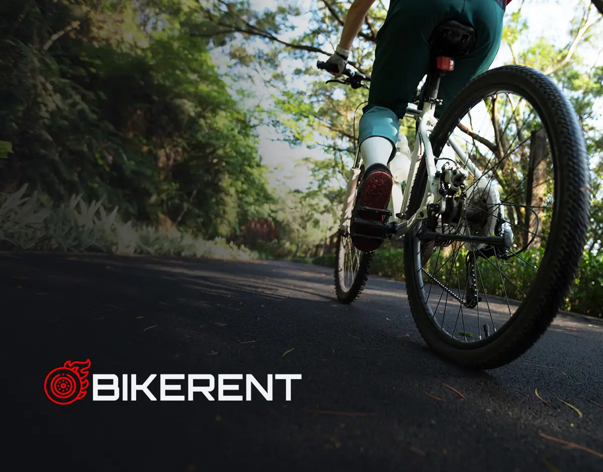 BikeRent: logo z czerwonym sygnetem koła na ciemnym zdjęciu rowerzysty na leśnej drodze
