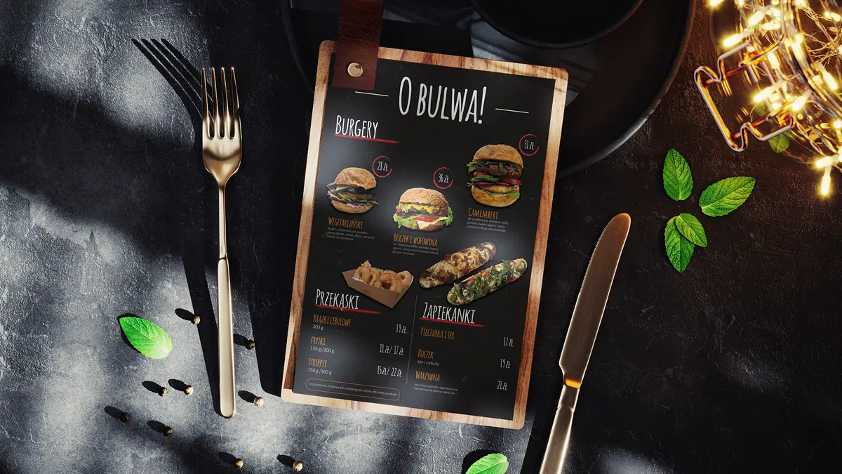 O Bulwa: menu na drewnianej desce na ciemnym stole obok widelca, noża i liści
