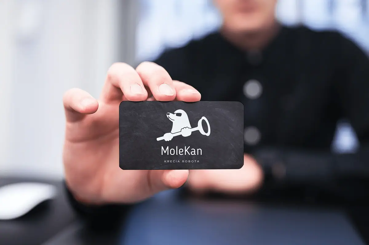 MoleKan: dłoń trzymająca grafitową wizytówkę z logo kreta i napisem MoleKan