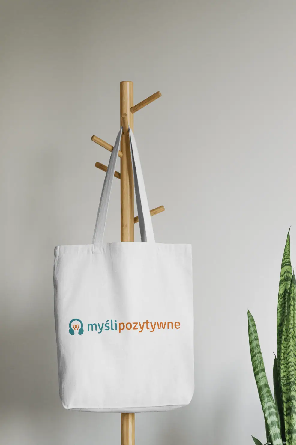 Myśli Pozytywne: logo w turkusie i pomarańczu na białej torbie zawieszonej na drewnianym wieszaku