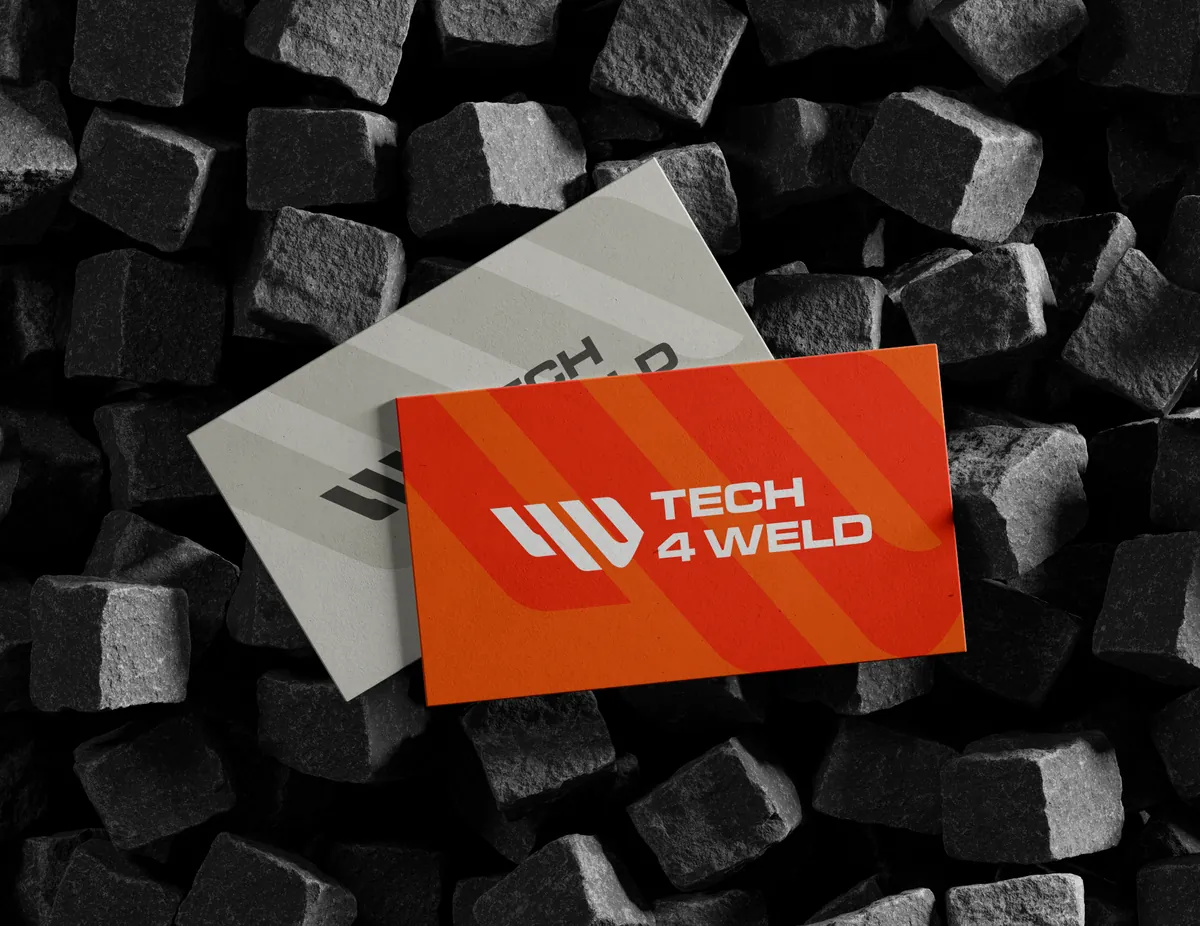 Tech 4 Weld: pomarańczowa i szara wizytówka z logo na stosie czarnych kamieni